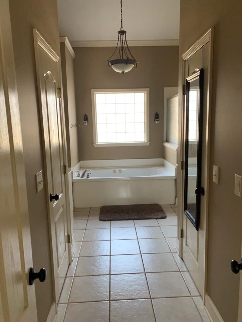 Tan-colored bathroom hallway leading up to a white bathtub