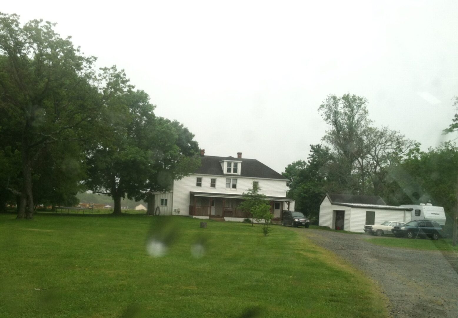 Faraway POV of a white two-story house with an attic in a wide field