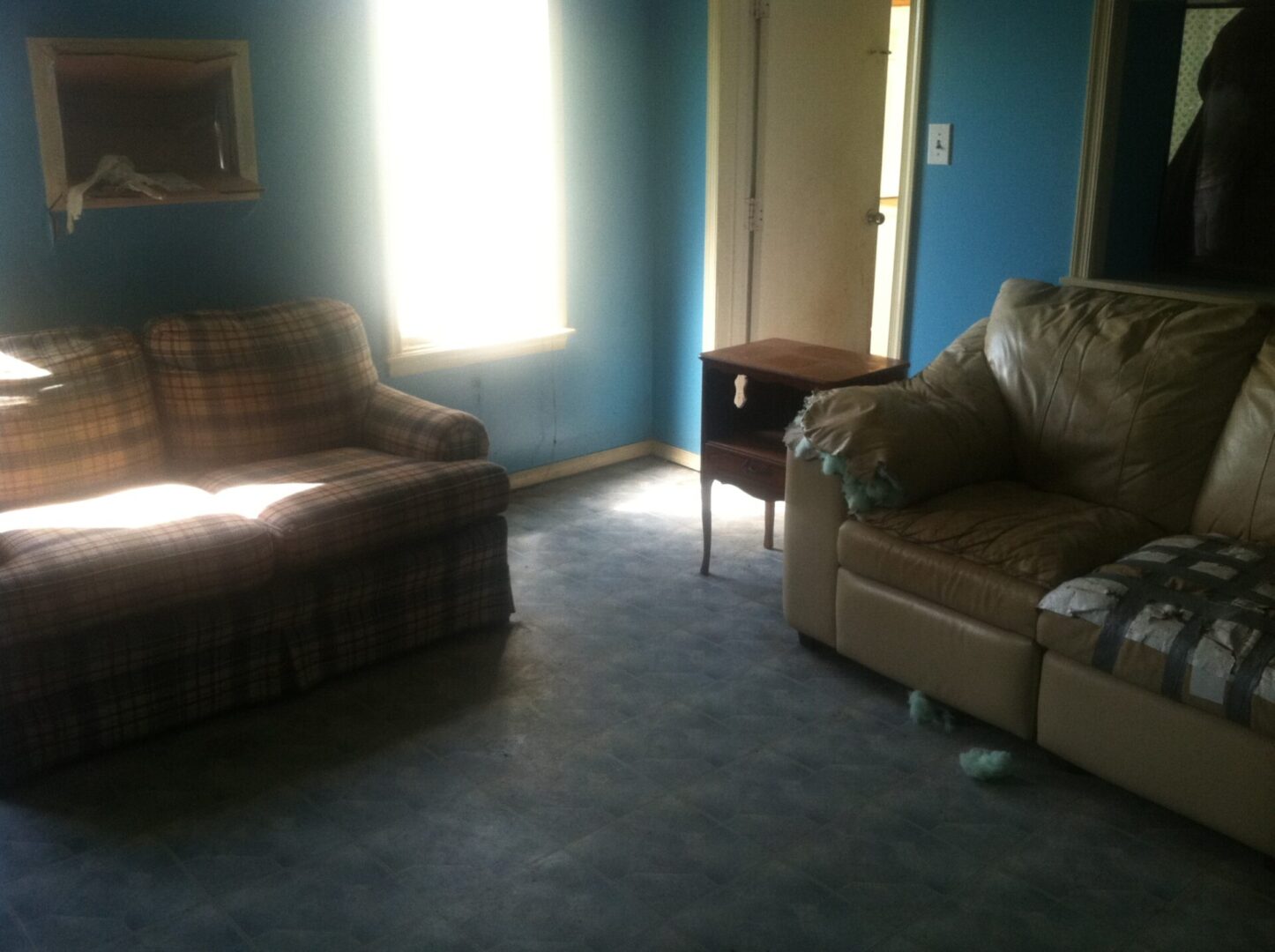 Blue living room interior with a checkered couch and a damaged leather sofa