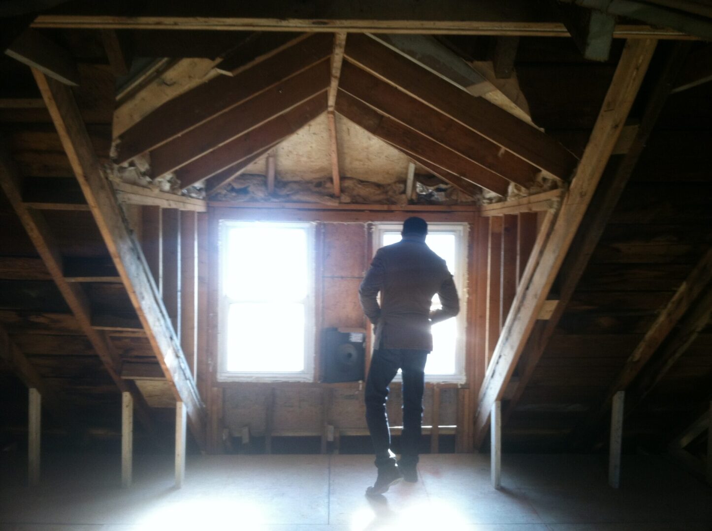Man standing in front of two windows inside the structural food framing of a house