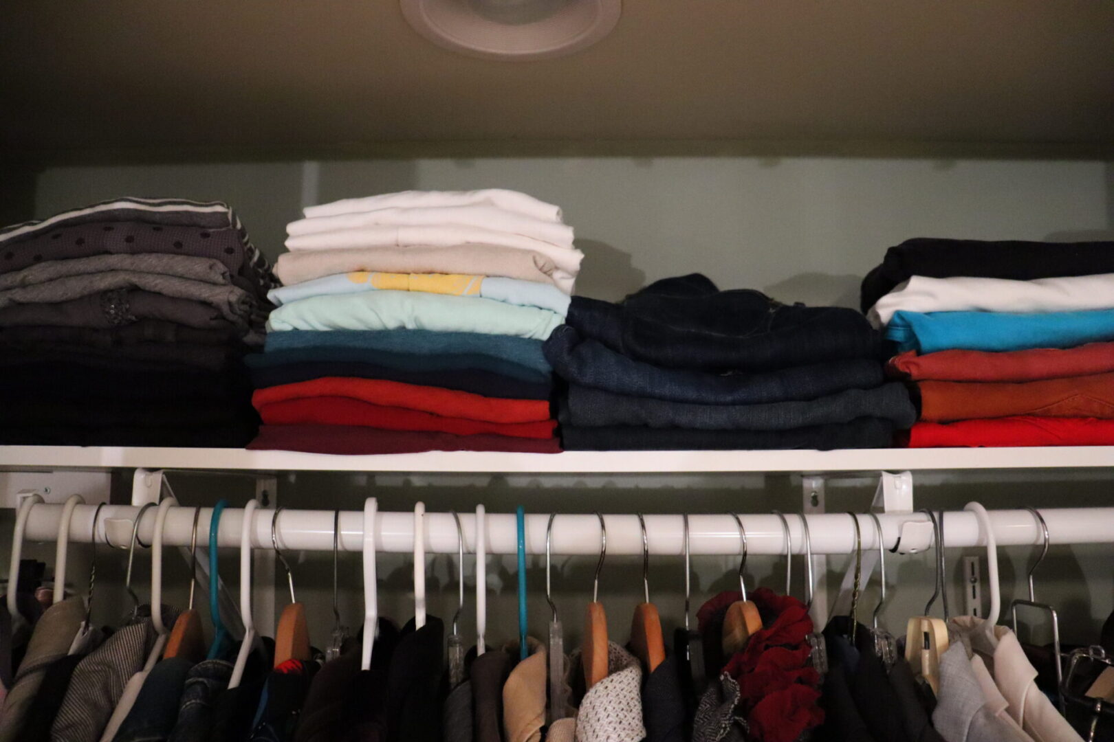 Shelf with folded clothes on top of a clothes hanger rod